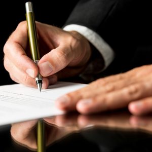 Closeup of male hand signing legal or insurance document on black desk with reflection.